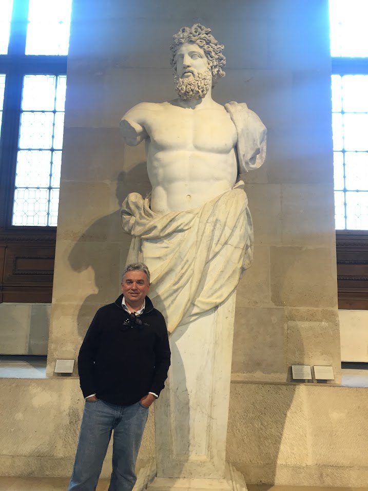 Patrick Searcy standing beside a classical marble statue in a museum gallery